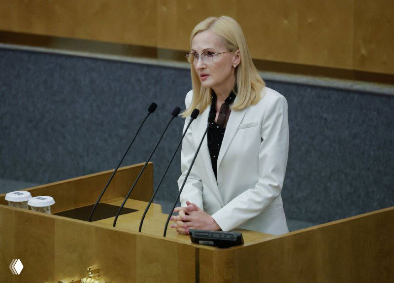 Женщина у трибуны в зале заседаний Госдумы выступает с докладом у микрофонов; кадр иллюстрирует обсуждение поправок к Уголовному кодексу по диверсии и терроризму.