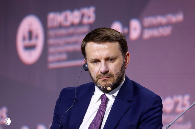 Портрет мужчины с небольшим выражением бороды на фоне сцены форума: наушник-переводчик, профессиональная панельная дискуссия, официальная атмосфера