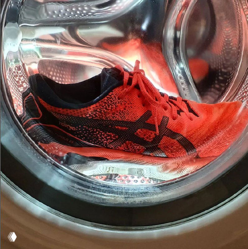 Красные беговые кроссовки внутри барабана стиральной машины, шнурки развязаны, иллюстрация риска стирки обуви.