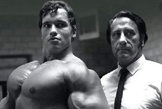 Чёрно‑белая историческая фотография: массивный бодибилдер в первом плане и мужчина в костюме рядом, ретро-атмосфера тренерских практик и формирования телесной культуры.