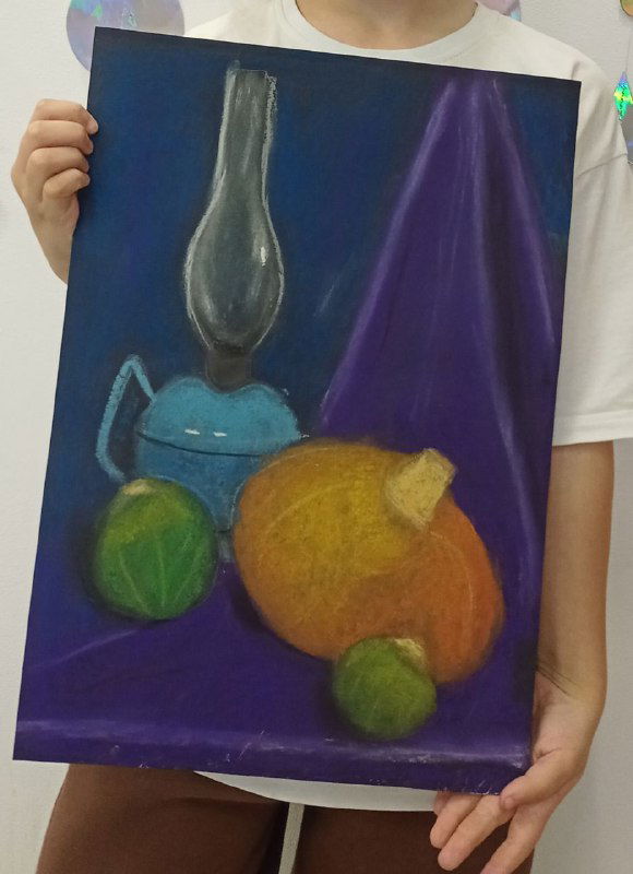 Учебная работа ребёнка 7–8 лет: натура сухой пастелью на синем фоне с лампой и оранжевым плодом, изображение держит ученик перед собой.