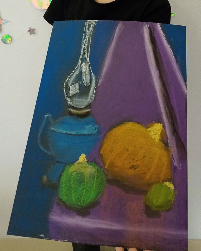 Работа ребёнка 7–8 лет: сухая пастель, синий и фиолетовый фон, лампа и тёплые оранжевые и зелёные фрукты, лист держит ученик.