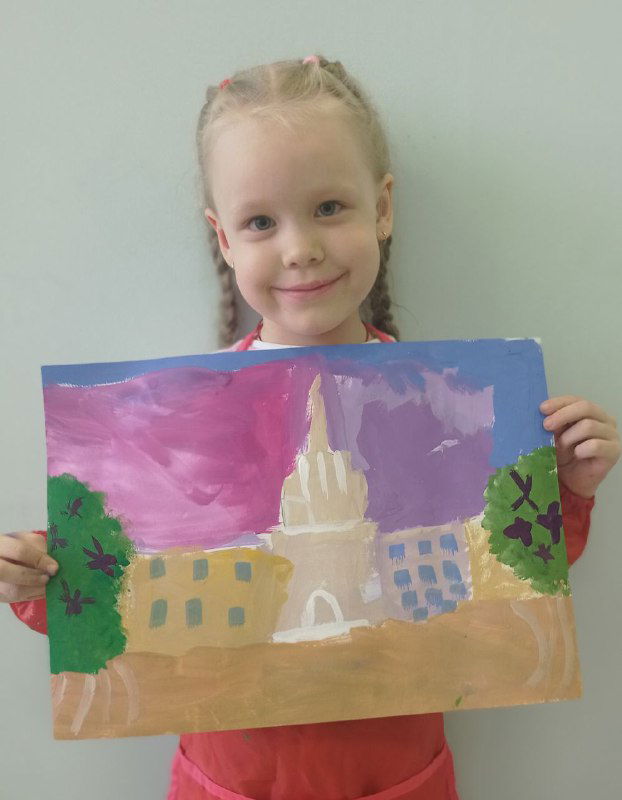 Девочка в розовом платье демонстрирует пейзаж с архитектурной доминантой и цветным небом; работа снята в классе возле декоративных элементов.