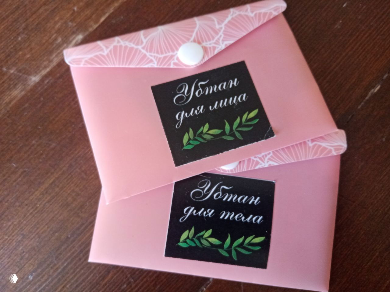 Две розовые упаковки-конверта с наклейками «Убтан для лица» и «Убтан для тела», аккуратно сложенные на деревянной поверхности, готовые к отправке.