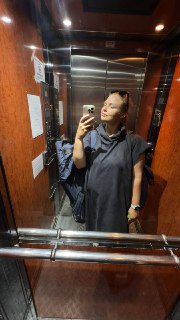 Человек в лифте делает селфи в спортивной одежде с рюкзаком на плече, видны зеркальные панели, поручни и панель управления лифта перед выездом.
