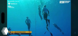 Подводный кадр с соревнований по фридайвингу: несколько спортсменов спускаются вдоль буйка в синей воде, кадр иллюстрирует соревновательную обстановку и судейские решения.