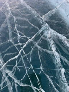 Сетчатая структура трещин в толще льда, пересекающиеся линии и прозрачные мостики льда, контрастирующие с тёмной глубиной под ним.