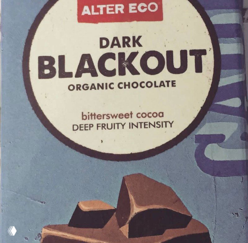 Крупный план упаковки тёмного шоколада с надписью «Dark Blackout»: кусочки шоколада на голубой фоновой этикетке.