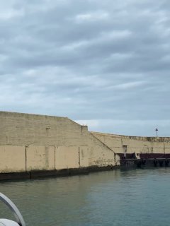 Бетонная пристань и спокойная морская гладь под пасмурным небом, вид с лодки на береговую стену в Сочи перед стартом.