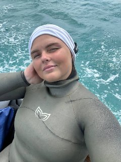 Крупный план фридайвера в гидрокостюме и головном накрытии, на фоне моря с небольшой волнением, после нырка.