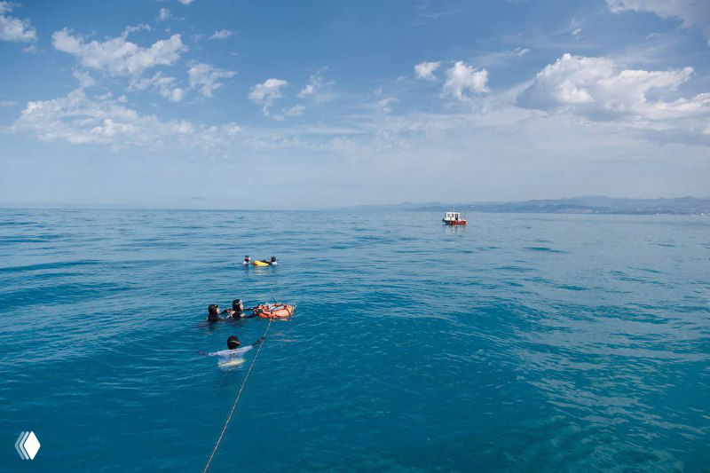 Вид сверху на открытое Черное море: спасательные лодки и группа фридайверов на поверхности во время соревнований в Сочи.