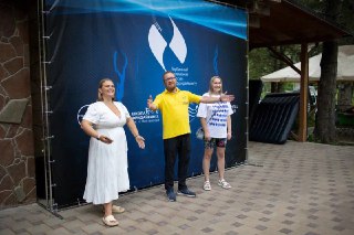 Три человека рядом с баннером чемпионата: организаторы и участник на площадке, атмосфера официального открытия и награждения соревнования