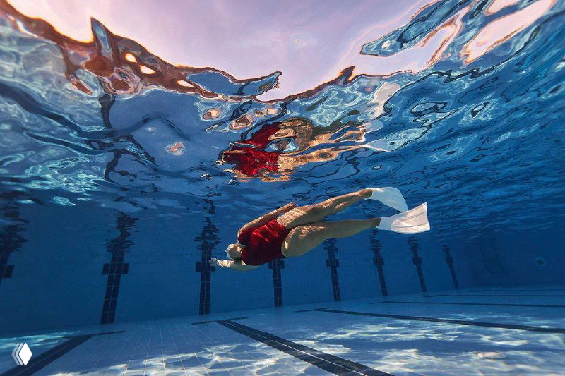 Ныряющий фридайвер под водой в бассейне в моноласте; вид снизу и поверхность воды сверху, тренировка дыхания и погружений в контексте рубрики.