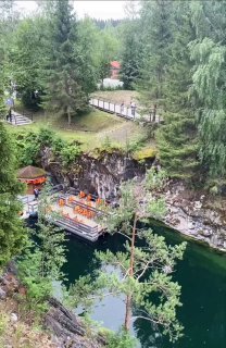 Вид сверху на скальный каньон с зелёной водой, деревянной смотровой площадкой у воды, лесистые склоны и прогулочная дорожка.