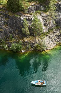 Лодка на изумрудной воде у скалистого берега карьера, вид сверху; спокойная летняя сцена с элементами фридайв-мероприятия.