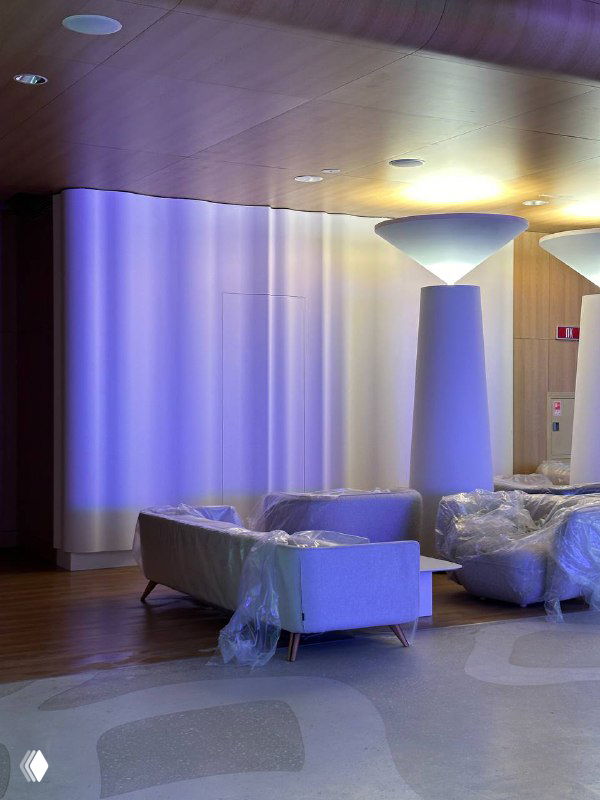 Зал с мягкой подсветкой и мебелью в плёнке, кадр показывает стадию подготовки интерьера и завершающие работы перед уборкой