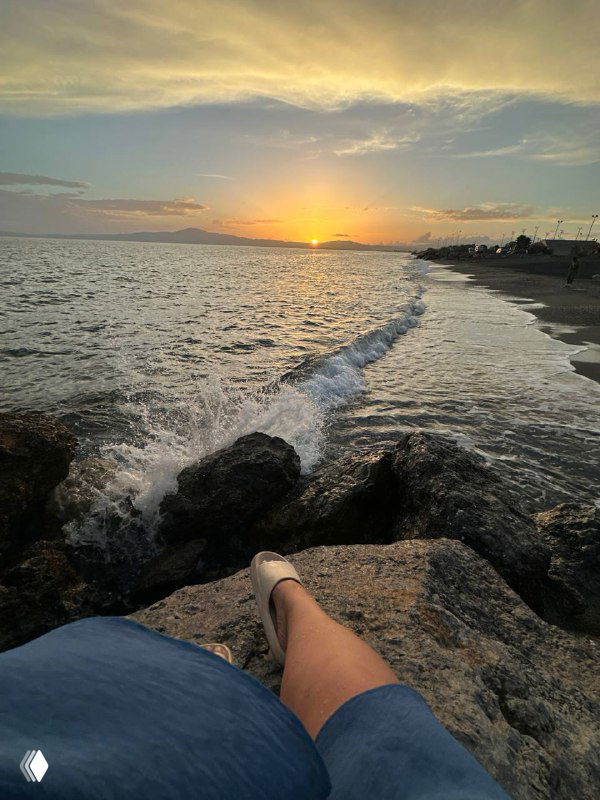 Закат на sunset point: вид на море с волнами и береговыми камнями, кадр от первого лица с ногами автора на переднем плане.