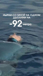Фридайвер на поверхности спокойного моря в очках, кадр из видео: видно лицо, гладь воды и надпись о погружении на −92 метра.