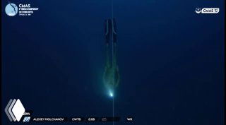 Подводный кадр трансляции: фридайвер опускается вдоль троса в тёмно-синей воде; виден луч камеры, наложение таймера и логотипы трансляции.