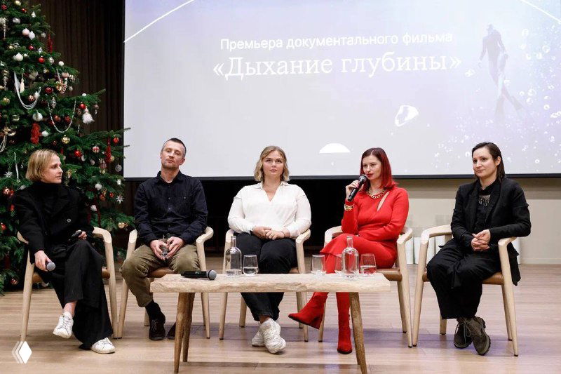 Панельная сессия на закрытой премьере документального фильма «Дыхание глубины»: участницы на сцене, фон с названием фильма и праздничная ёлка рядом.