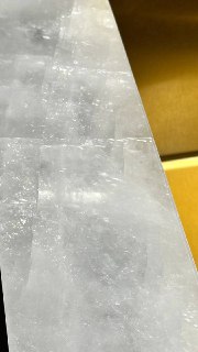 Крупный план края столешницы рядом с золотой раковиной, видна текстура плит, тонкие световые переливы и швы между элементами.