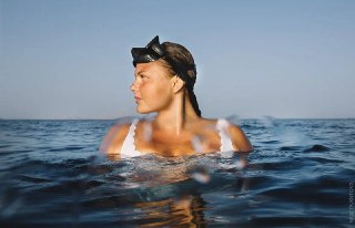 Женщина в море с маской для фридайвинга на лбу, на поверхности воды; фото передаёт спокойствие и связь с дыханием.