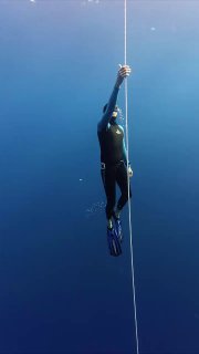Фридайвер поднимается по веревке в глубокой синей воде, видны ласты и часть тела, акцент на глубине и спокойствии моря.