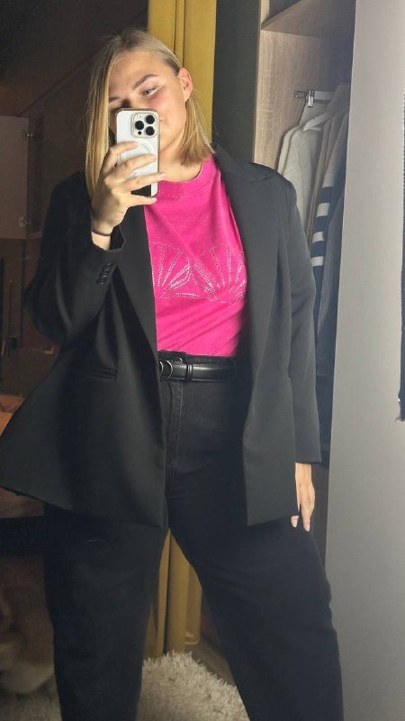 Авторка в зеркале в комплекте с черным пиджаком и ярко-розовой футболкой с блестящим принтом в виде ракушек, снимок в примерочной.