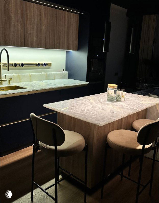 Ониксовая столешница в кухонной зоне с подсветкой и барными стульями; видна ледяная бело‑серо‑перламутровая текстура и сияние камня.