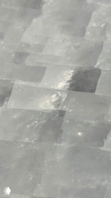 Крупный план мозаичной поверхности оникса: полупрозрачные белые и серые пластины, заметен характерный блеск и пересекающиеся швы камня.