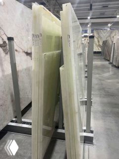 Листы оникса на складе: вертикальные пластины камня на стойках, представлены разные оттенки и текстуры до обработки и установки.