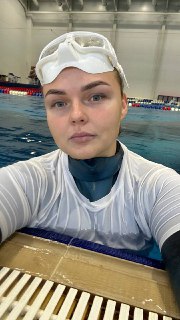 Селфи фридайвера у бортика бассейна: лицо в очках для плавания на лбу, гидрокостюм и мокрая футболка, фон дорожек и воды.