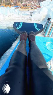 Кадр с лодки: ноги в гидрокостюме на фоне льдин и берега Байкала, термос на борту; иллюстрация видео, фиксирующего звуки озера и ледовую обстановку.