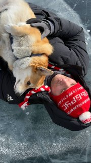 Бухта прижимается к человеку в красной шапке и тёплой одежде на льду Байкала, снимок крупным планом, видно текстуру льда.