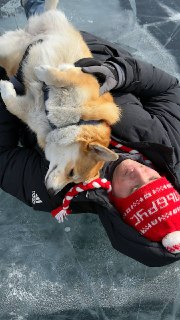Человек в теплой одежде лежит на ледяной поверхности, обнимает собаку — сцена тепла и доверия посреди холодного Байкала.