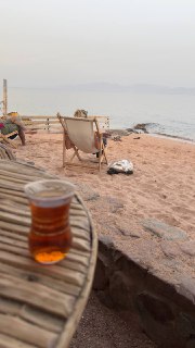 Стакан чая на плетёном столике у песчаного берега; на заднем плане пустые шезлонги, море и тихий горизонт