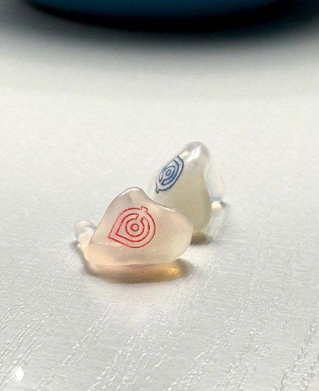 Пара индивидуальных силиконовых берушей на белой поверхности, видны логотипы и форма изделия — демонстрация внешнего вида и размера