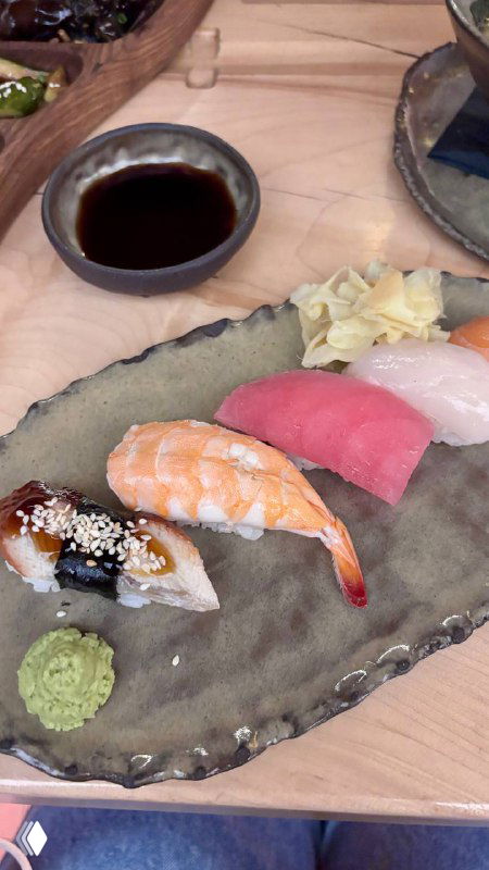 Плато с разными суши на керамической тарелке: креветка, лосось и тунец, рядом вазочка с соевым соусом, васаби и маринованный имбирь.