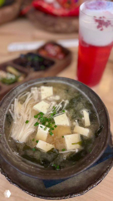 Глубокая миска мисо-супа с тофу, эноки и зелёным луком, чаша на деревянном столе в интерьере японского ресторана.