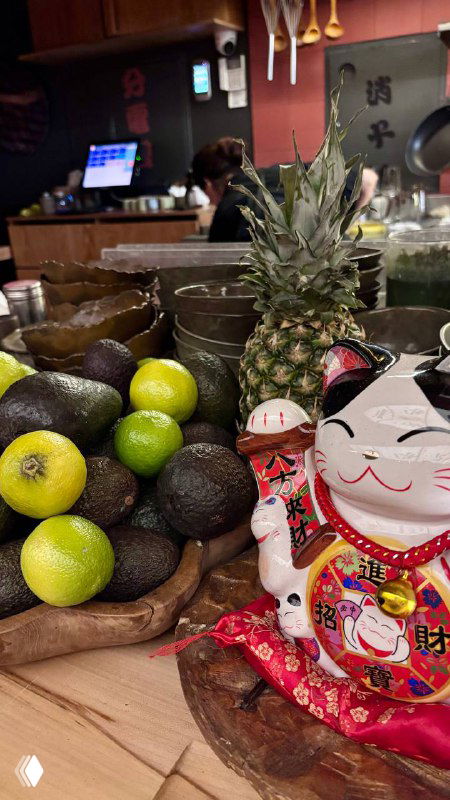 Декоративная композиция на стойке: ананас, авокадо, лаймы и фигурка манэки-нэко — детализация оформления ресторана в японском стиле.