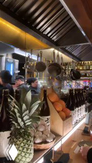 Открытая кухня и полки с бутылками саке, повара и подсобная зона видны за стойкой — атмосфера живой гастрономии.