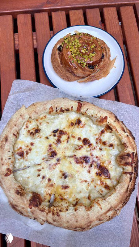 Небольшая пицца с тянущимся сыром и булочка с фисташковой крошкой на бумаге — подача из Mates, акцент на тесто и выпечку.