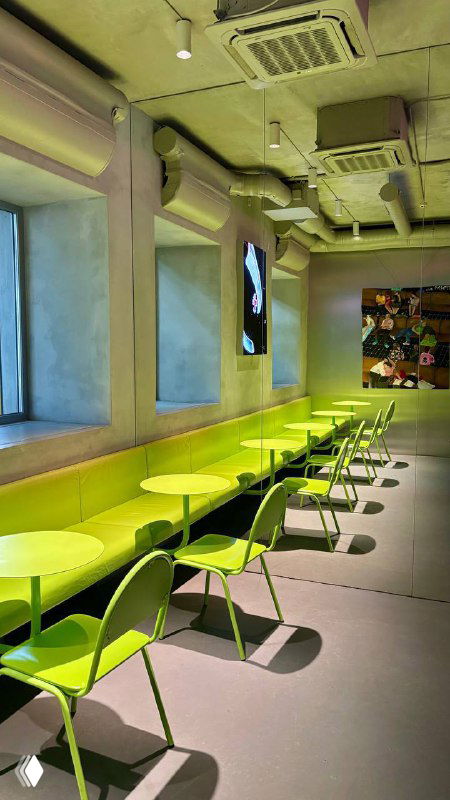 Узкий зелёный интерьер кофейни 2046 с рядом лаймовых столиков и стульев, минималистичная отделка и видимые воздуховоды на потолке.