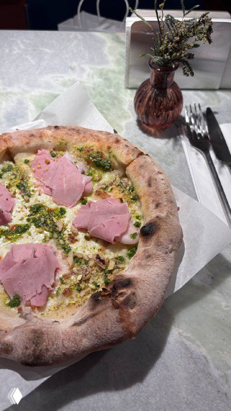 Крупный план неаполитанской пиццы на бумажной кальке: румяная корочка, ломтики розовой ветчины, зелёная посыпка и столовая сервировка рядом.