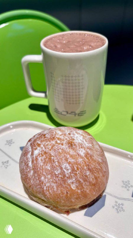 Какао в белой кружке и рядом итальянская булочка сфолья, присыпанная сахарной пудрой, на зелёном столе кофейни 2046.