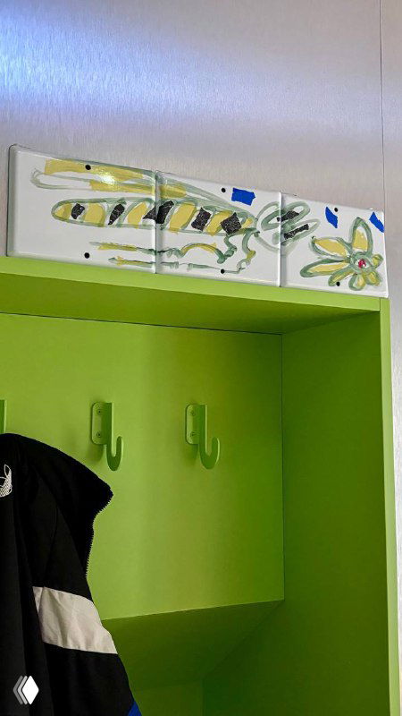 Зелёная гардеробная ниша с крючками и декоративными керамическими панно над ней в интерьере кофейни 2046, акцент на деталях оформления.