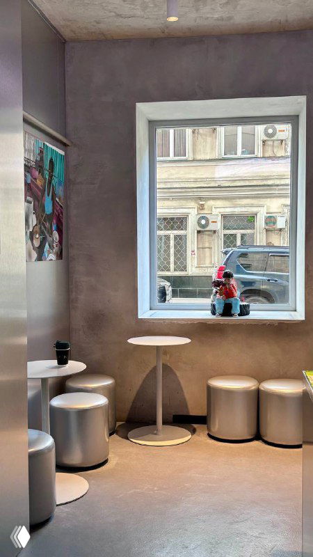 Уютный уголок у большого окна в кофейне 2046: столики, пуфы и вид на улицу через окно, художественные предметы на стене.