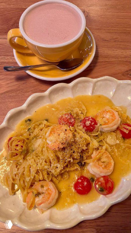 Тарелка лингвини с креветками и ярким чесночным соусом рядом с чашкой розового напитка — подача на веранде кафе Layerz в Москве.