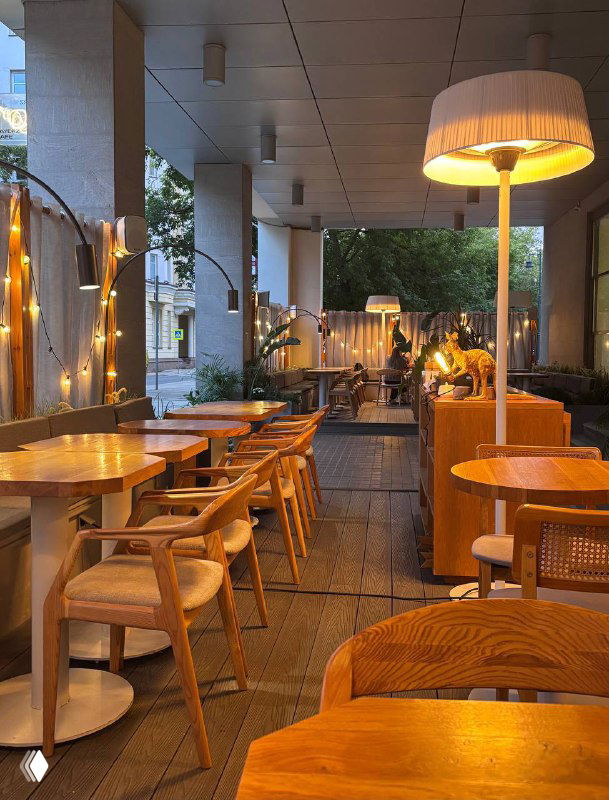 Уютная веранда кафе с деревянными столами, тёплой подсветкой и плетёными креслами — вечерняя атмосфера Layerz на Большом Кисловском переулке.