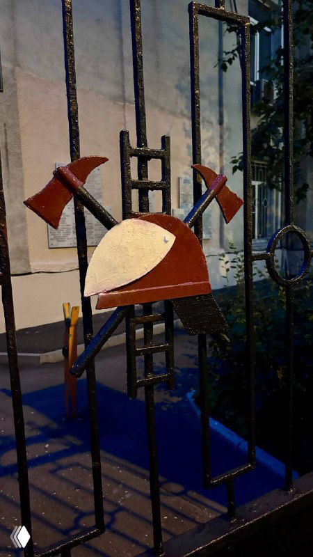 Граффити или арт-объект с изображением топоров и декоративных элементов на металлической ограде — уличное творчество района поблизости.